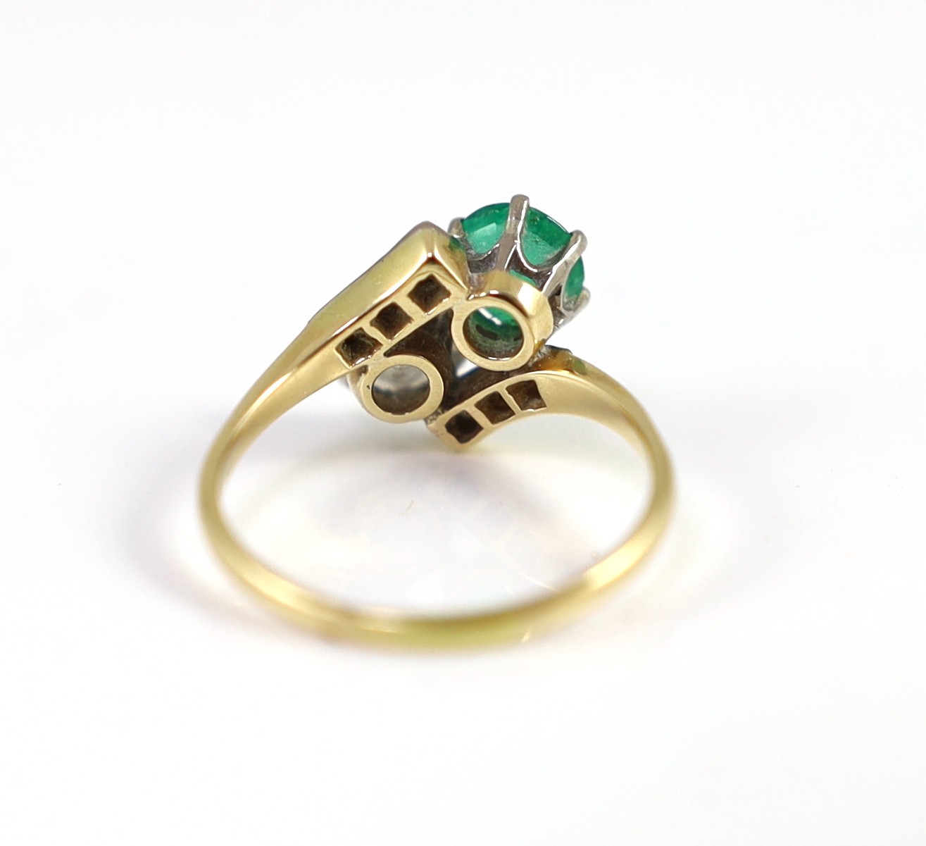 A gold, emerald and diamond set two stone cross-over ring, with diamond set shoulders